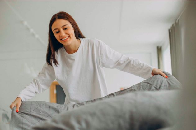 Mulher usando as dicas para deixar a cama bonita e arrumada do Grupo Wood.